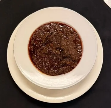A dish of rich brown meat sauce served in a white bowl on a plate.