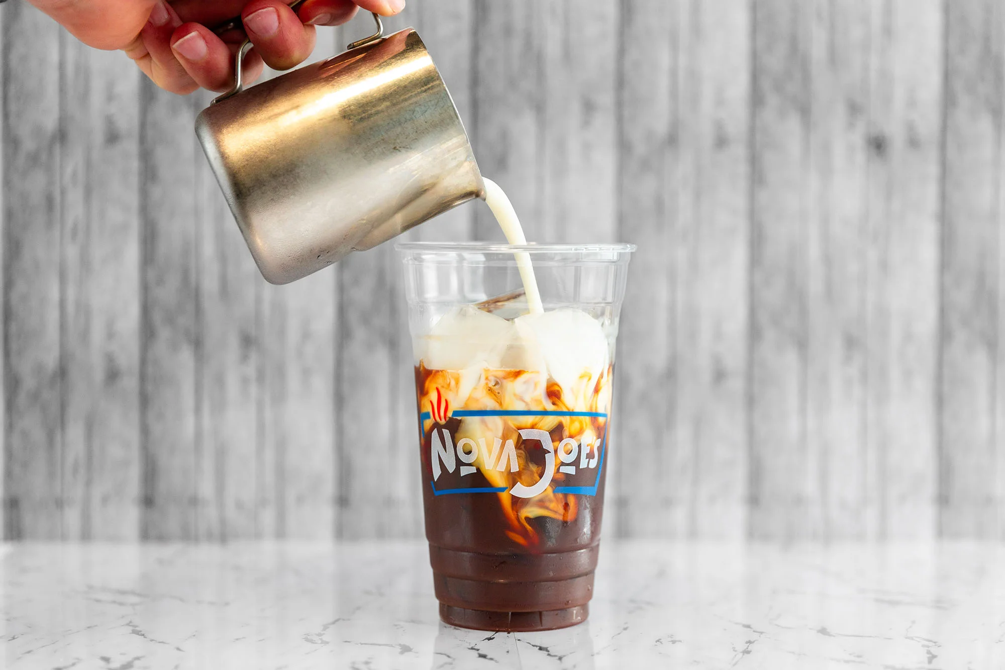 Cold cream being poured into an iced coffee.