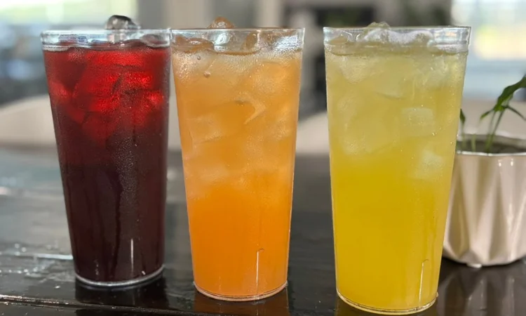 Three colorful drinks in clear cups filled with ice, featuring red, orange, and yellow beverages.