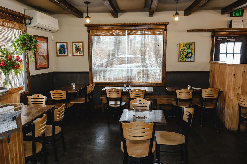 An inviting restaurant interior featuring wooden furniture, large windows, and decorative artwork on the walls.