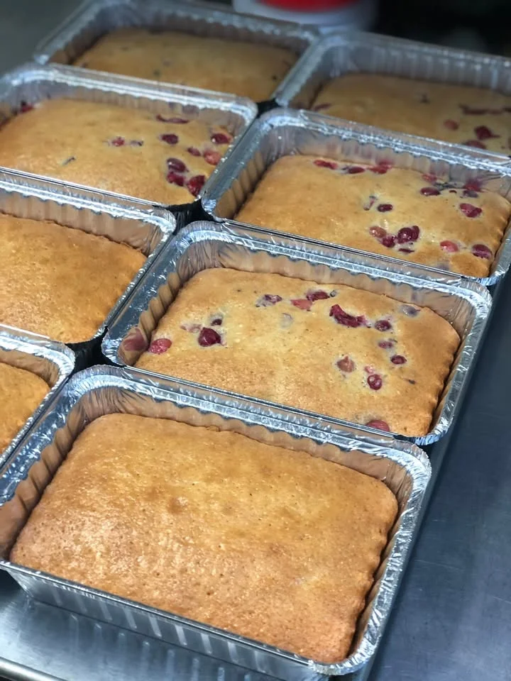 Several aluminum trays filled with freshly baked cakes, some with visible fruit pieces on top.