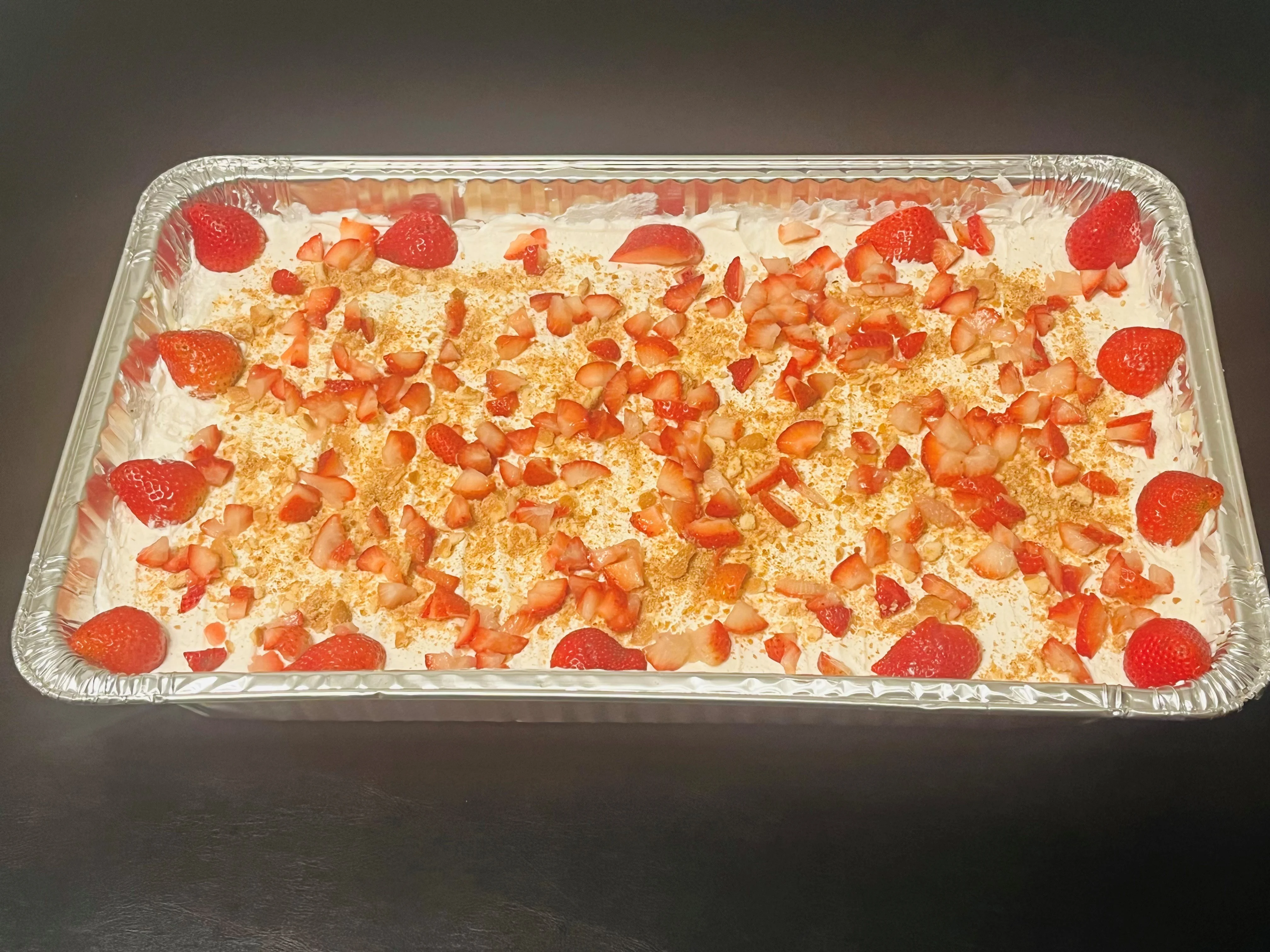 A dessert tray featuring a creamy layer topped with chopped strawberries and whole berries, perfect for summer gatherings.