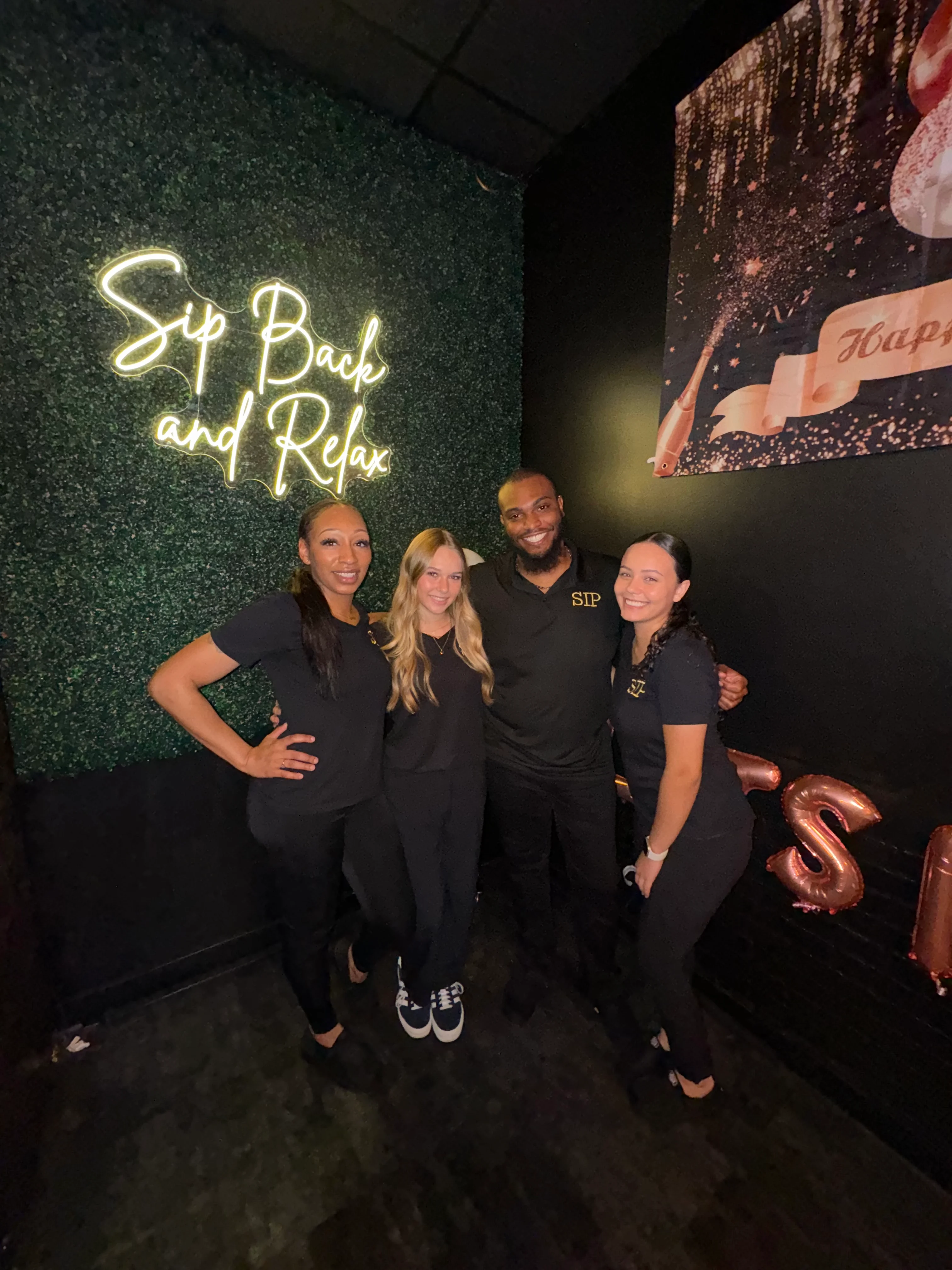 Staff posing in front of a neon sign at a cozy bar