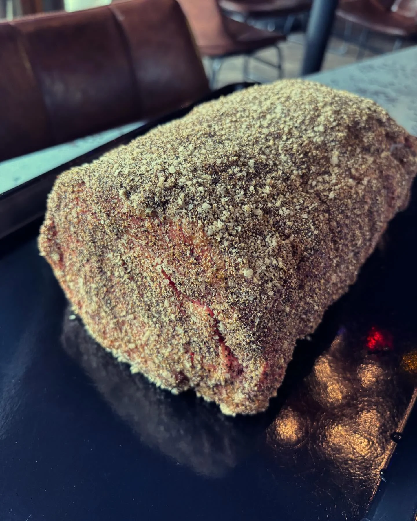 A seasoned meat loaf, coated with a layer of spices, resting on a surface.