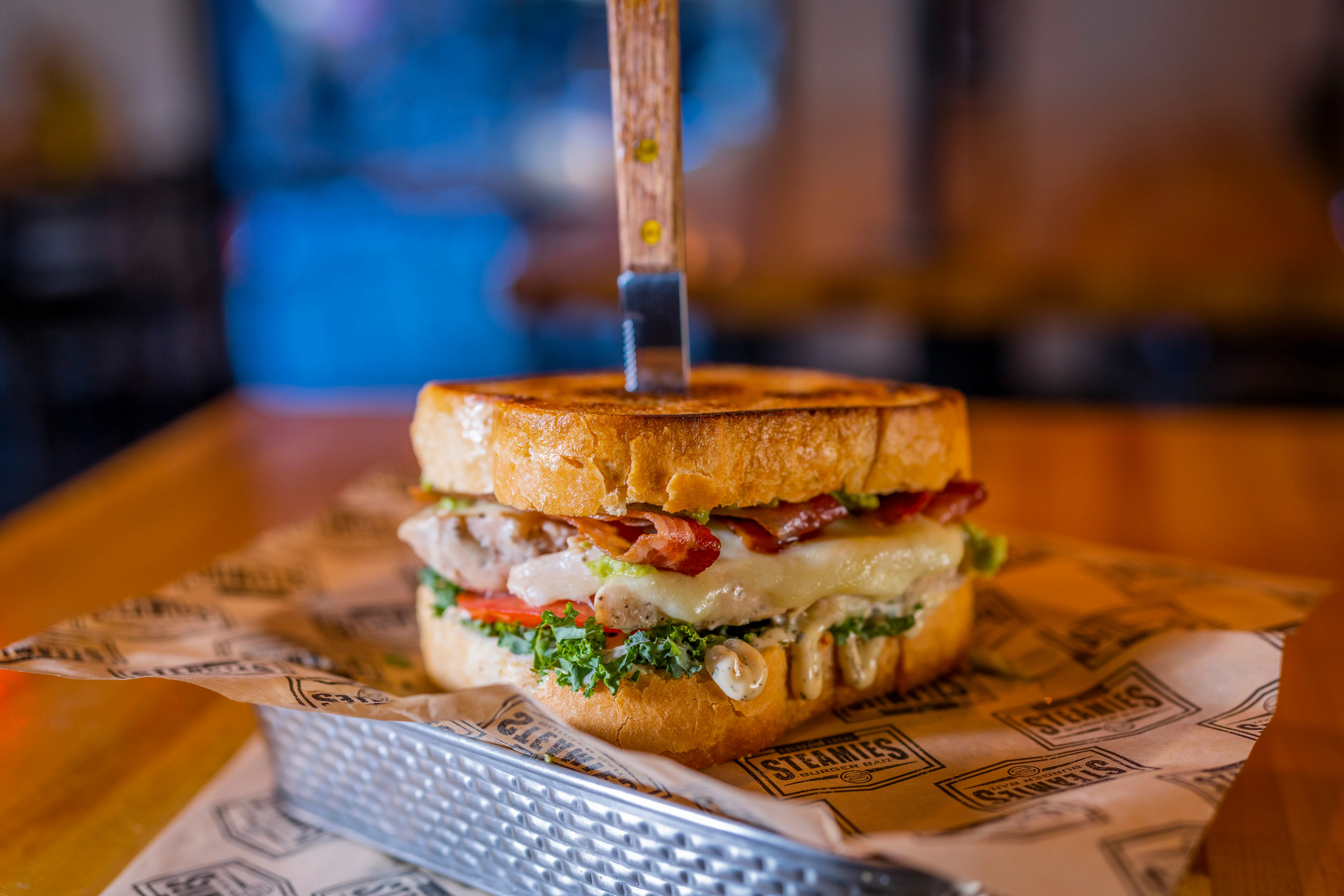 A hearty sandwich made with toasted bread, filled with meat, cheese, bacon, lettuce, and tomatoes, held together with a skewer.