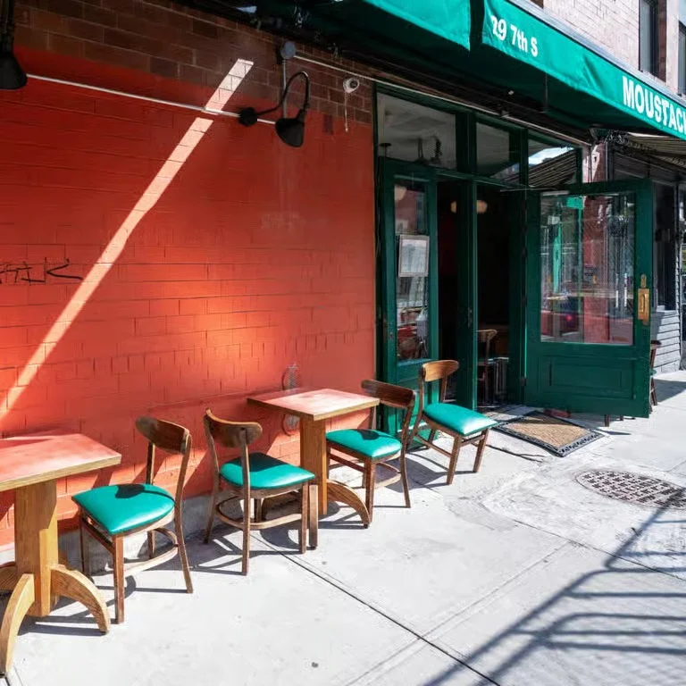 Outdoor seating area of a restaurant with green chairs and tables against an orange wall.