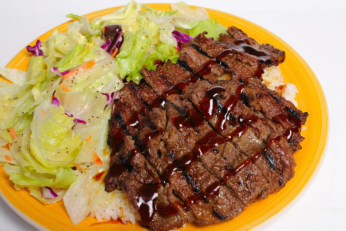 A colorful plate featuring grilled steak drizzled with sauce, accompanied by a side salad and rice.