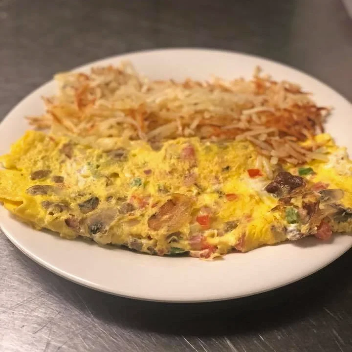 A fluffy omelette filled with colorful vegetables and mushrooms, paired with a generous portion of crispy hashbrowns on a white plate.