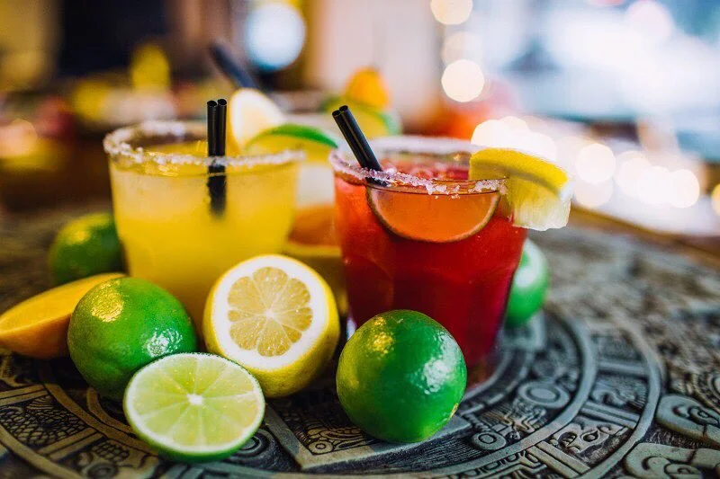 Two margaritas with salted rims and citrus fruits on an Aztec tray.