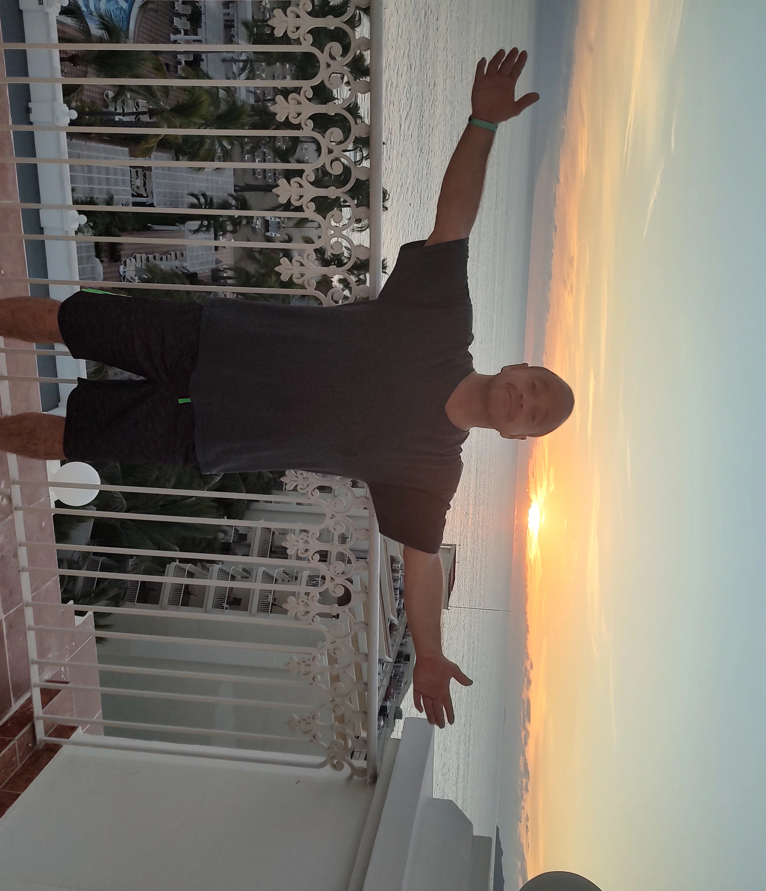 Person enjoying a sunset view from a balcony by the ocean