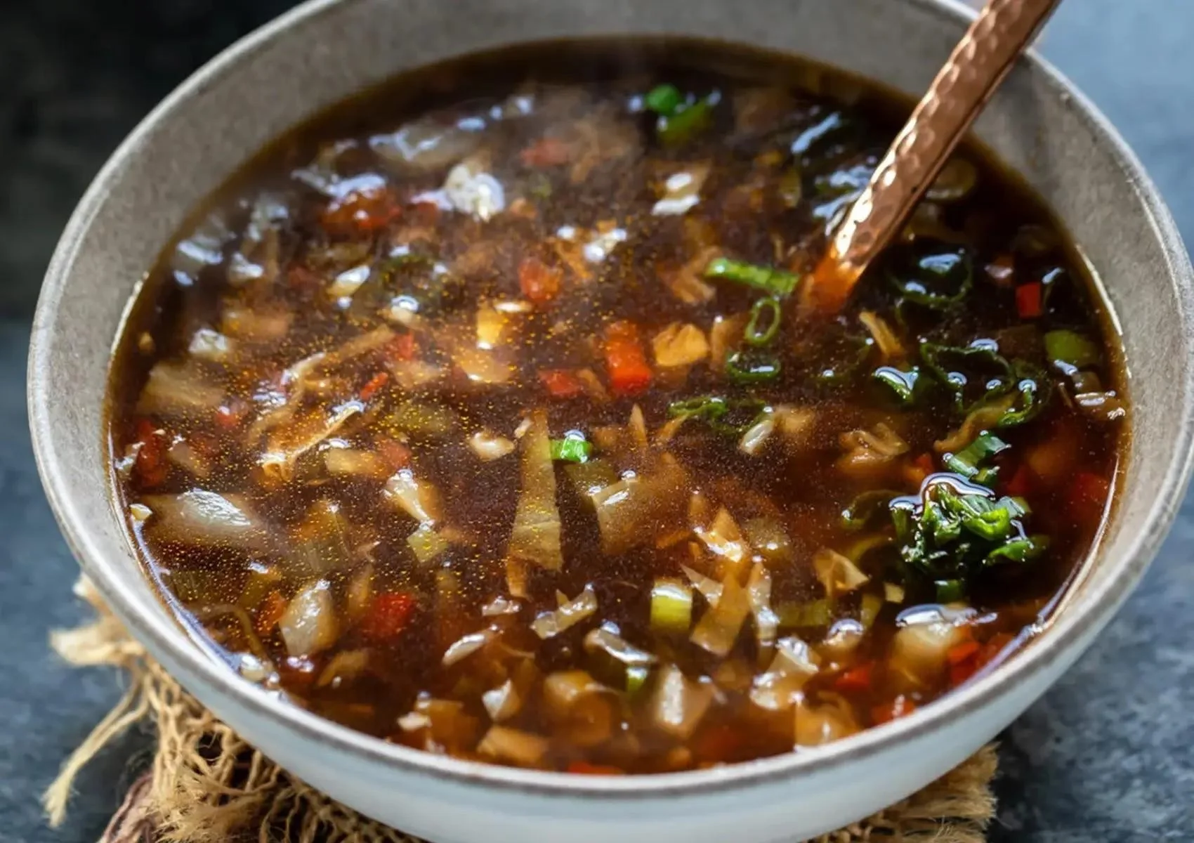 A bowl of hot and steaming vegetable soup, filled with a colorful mix of chopped veggies and herbs.