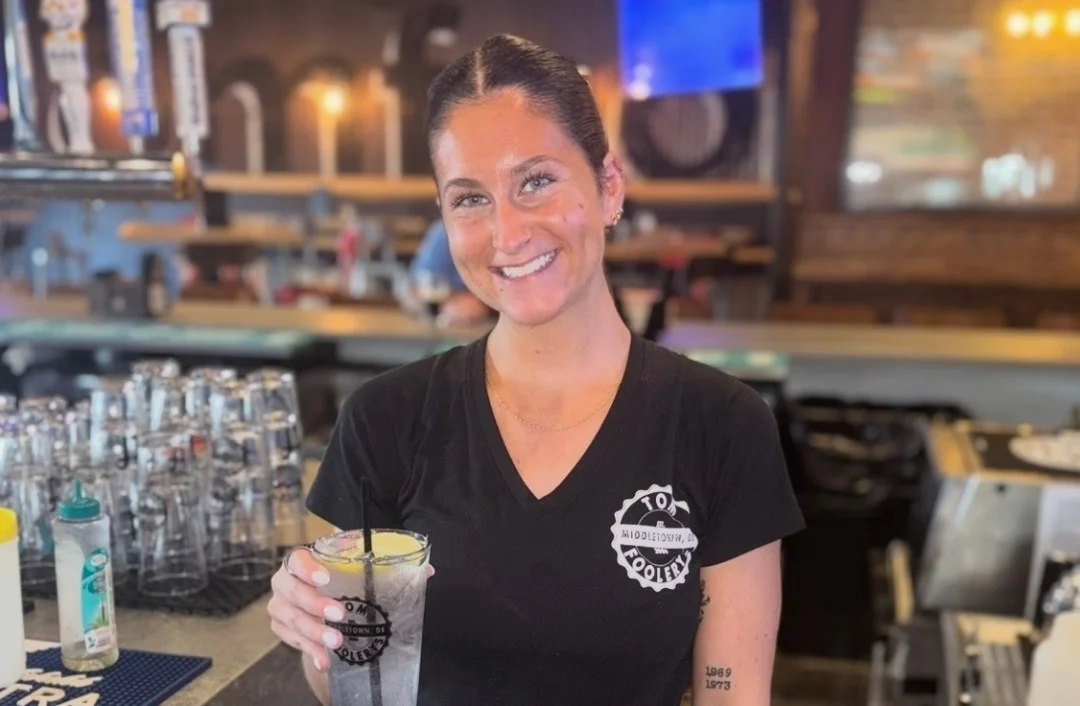 Bartender smiling with a cocktail at a lively bar