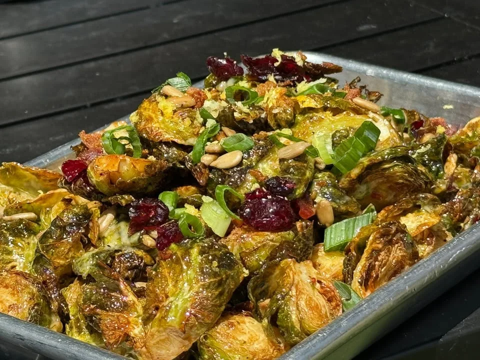 A tray of roasted Brussels sprouts topped with green onions, cranberries, and nuts, creating a colorful and appetizing side dish.