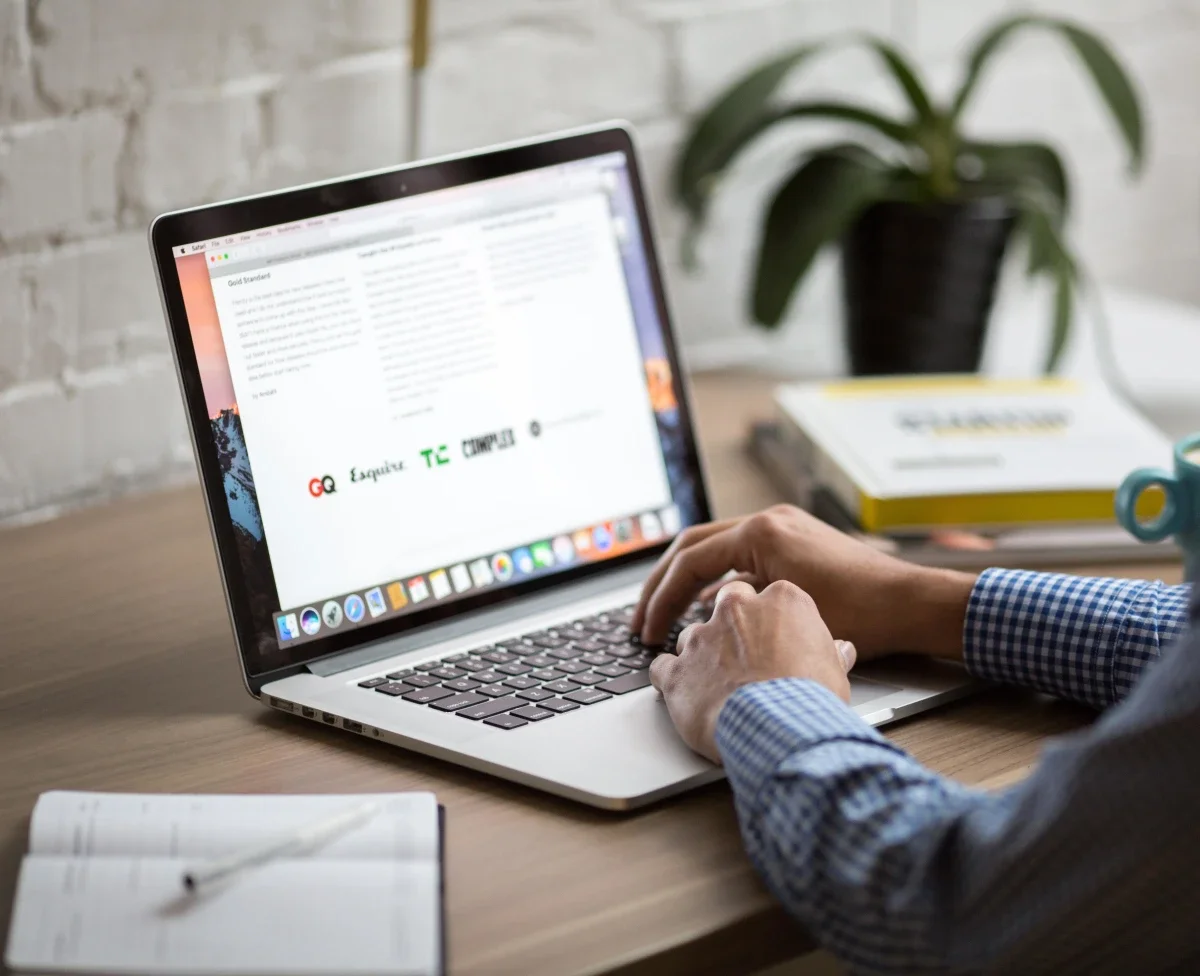 Person typing on a laptop at a wooden desk with a plant
