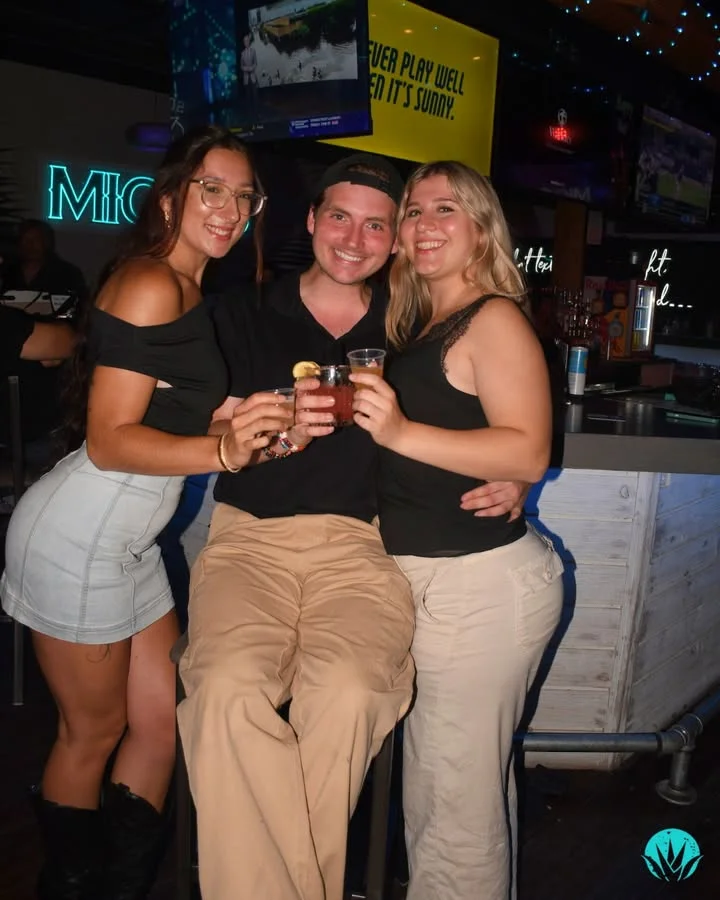 Three friends enjoying cocktails at a lively bar atmosphere.