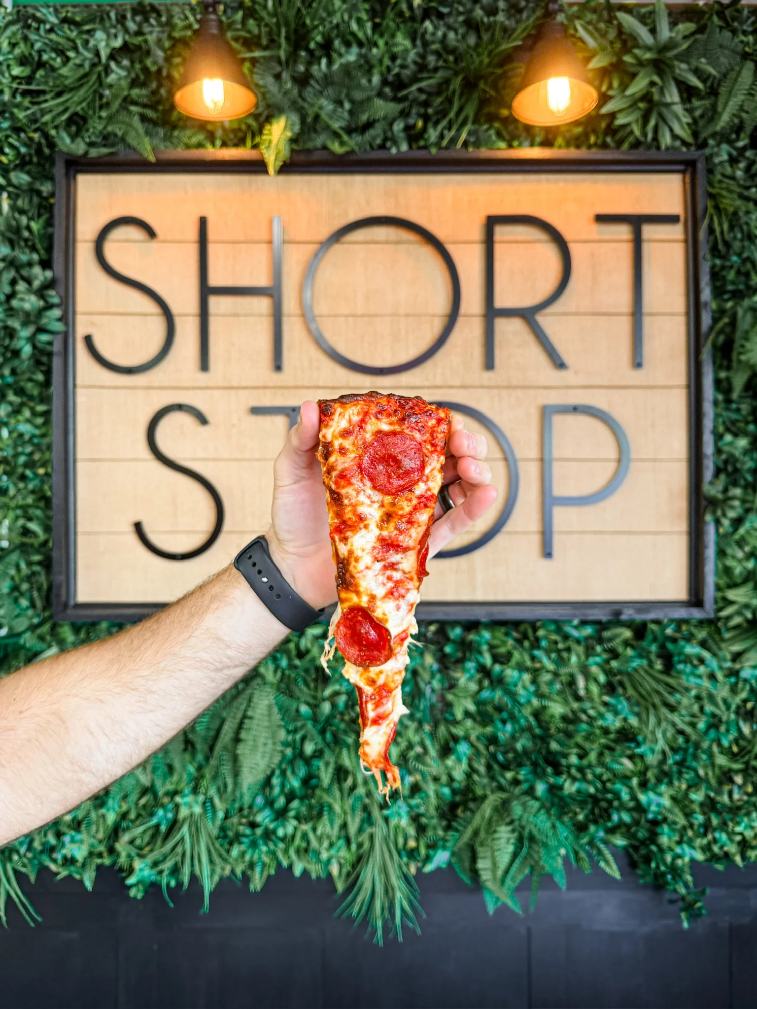 Pepperoni pizza slice held in front of a restaurant sign