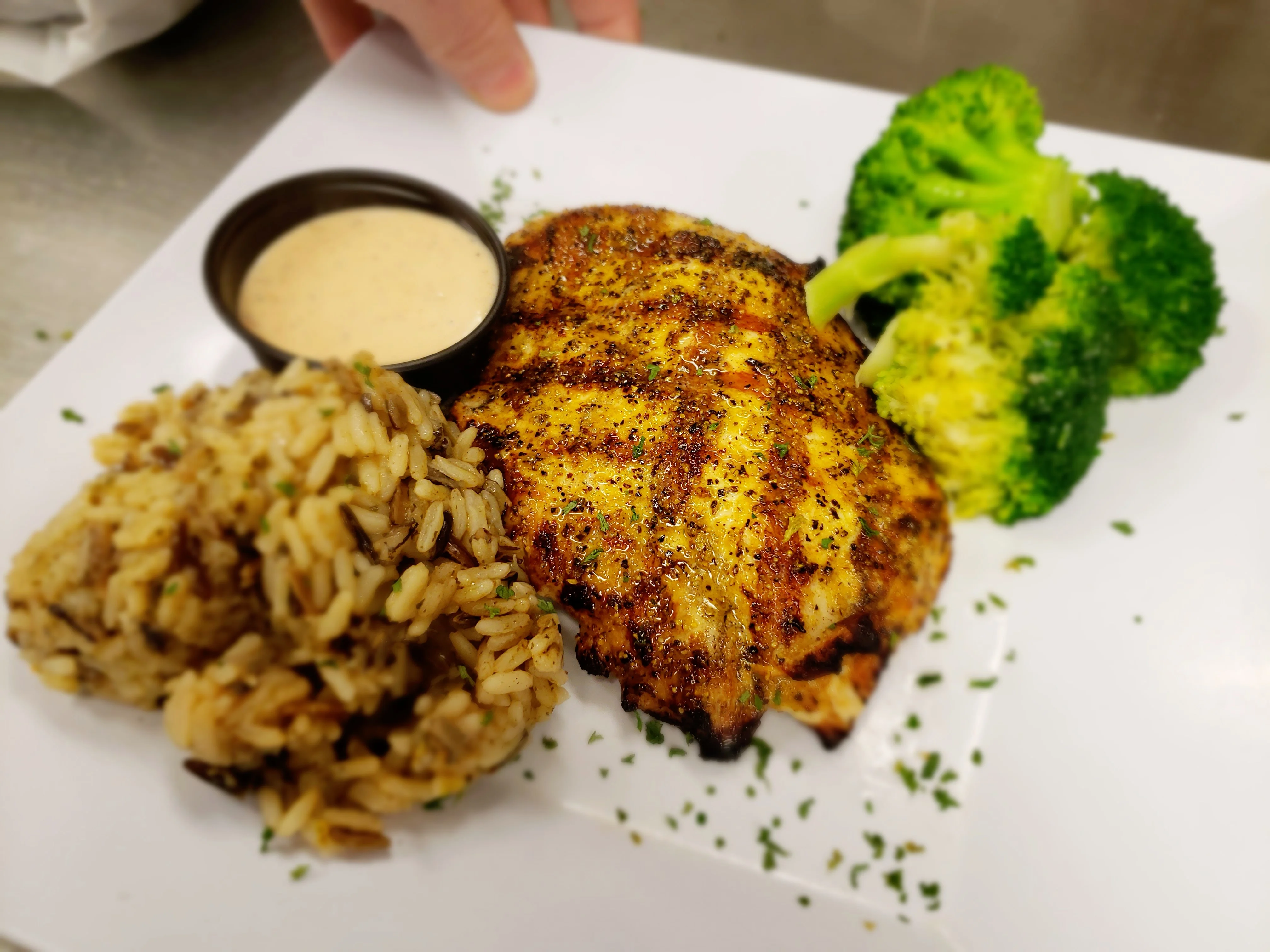 A plate of grilled chicken served with seasoned rice, fresh broccoli, and a side of dipping sauce.