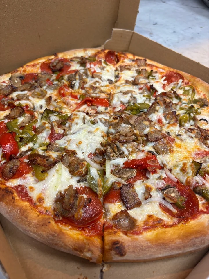 A meat and vegetable pizza topped with melted cheese, pepperoni, green peppers, and onions, served in a pizza box.