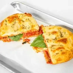 Handheld slice of pizza with a green topping, wrapped in paper for easy eating.