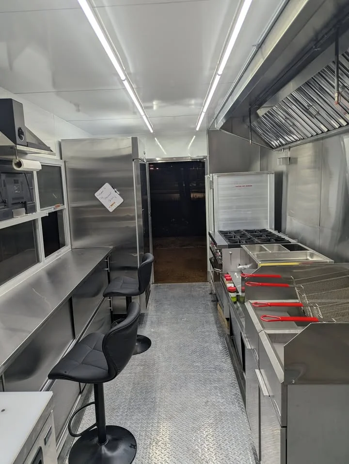 An interior view of a food truck kitchen featuring stainless steel equipment, cooking stations, and seating.