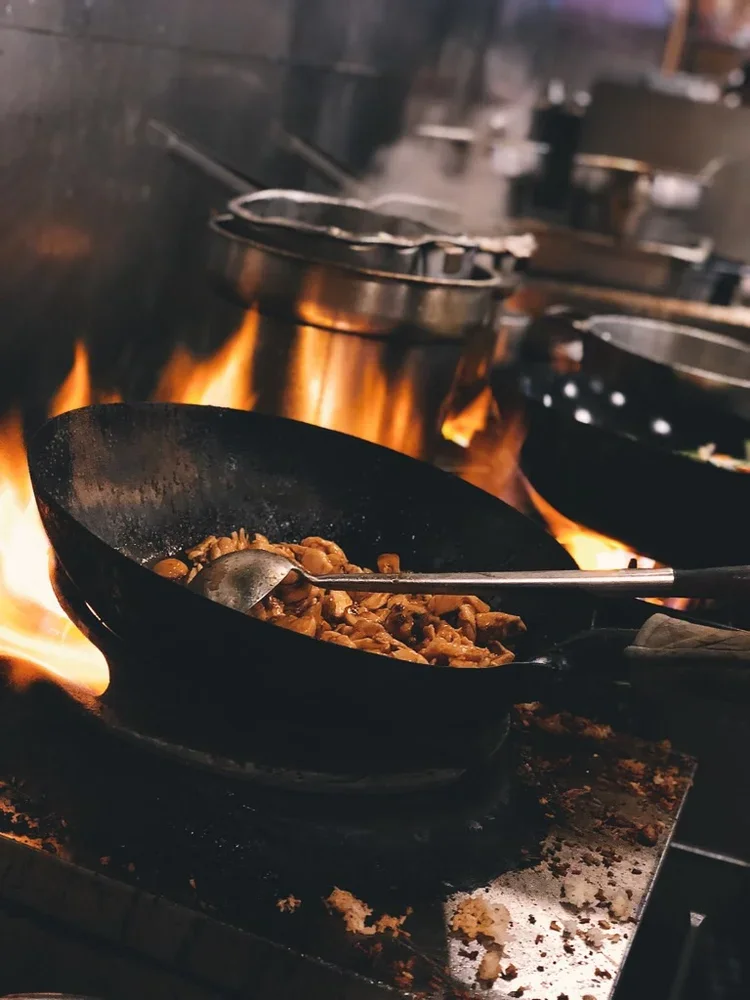 Wok cooking stir-fried vegetables over an open flame
