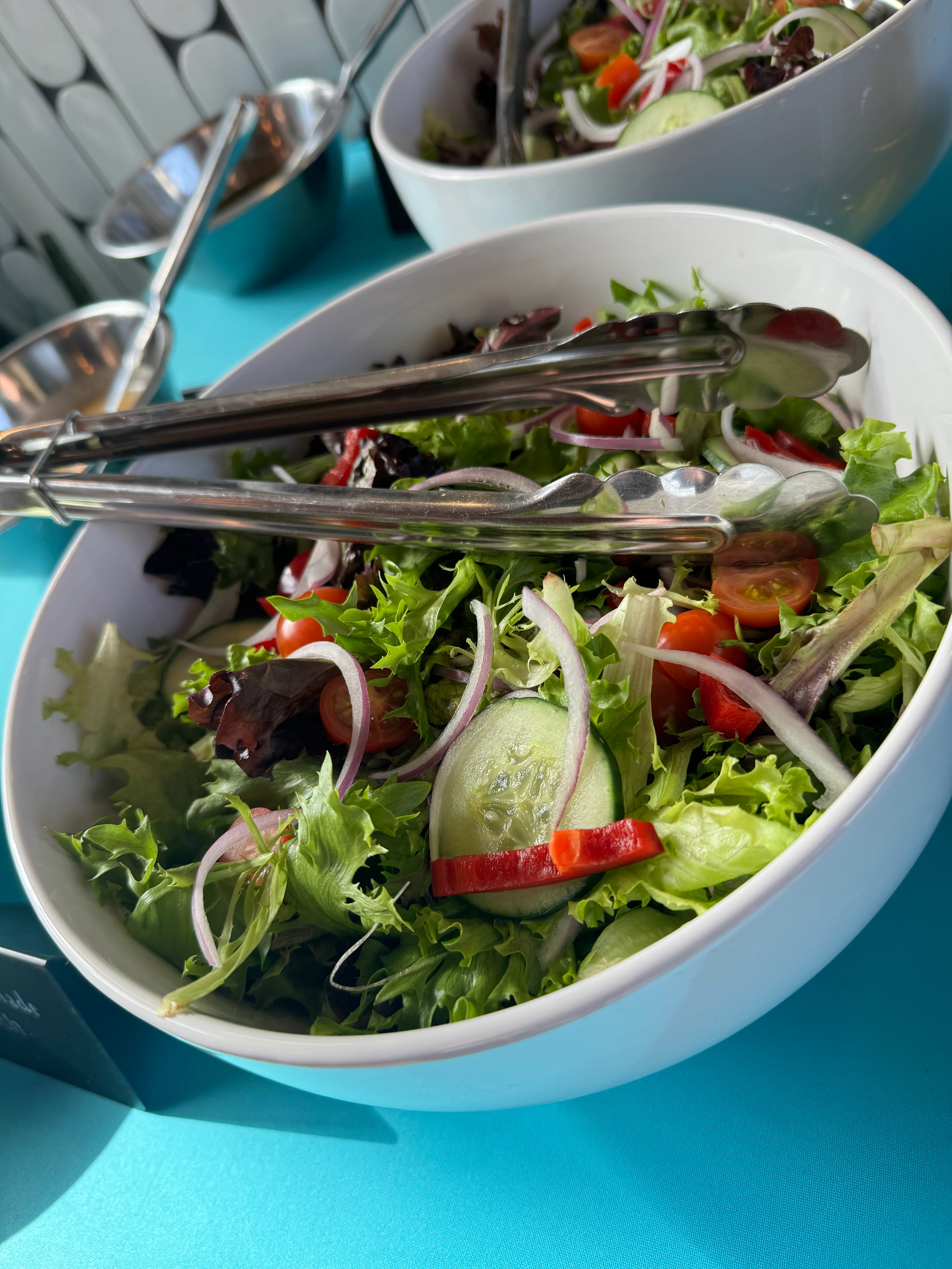 Fresh garden salad in a white bowl with tongs