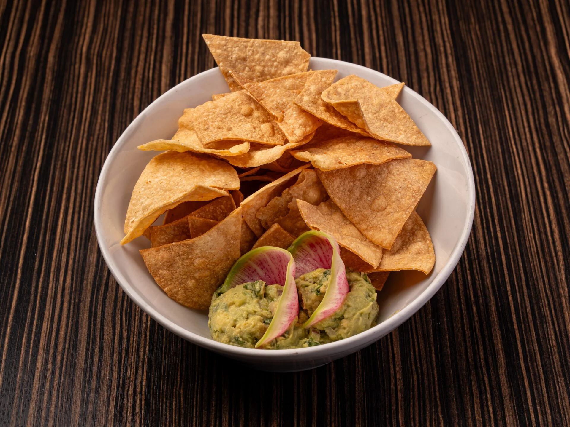 Crispy tortilla chips with guacamole and radish garnish