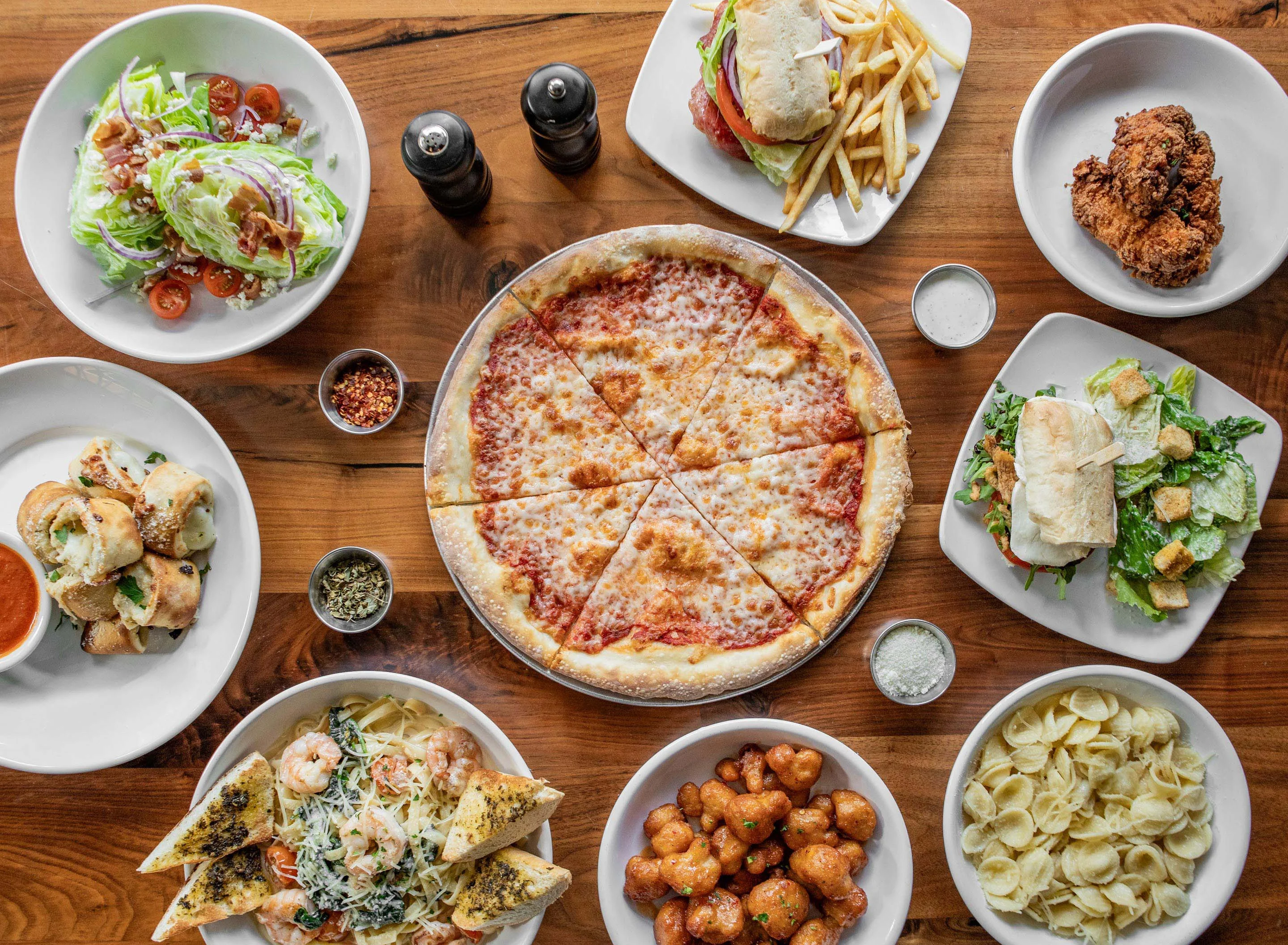 Overhead spread of Italian-American pizza, pasta, salads, wings, and sandwiches
