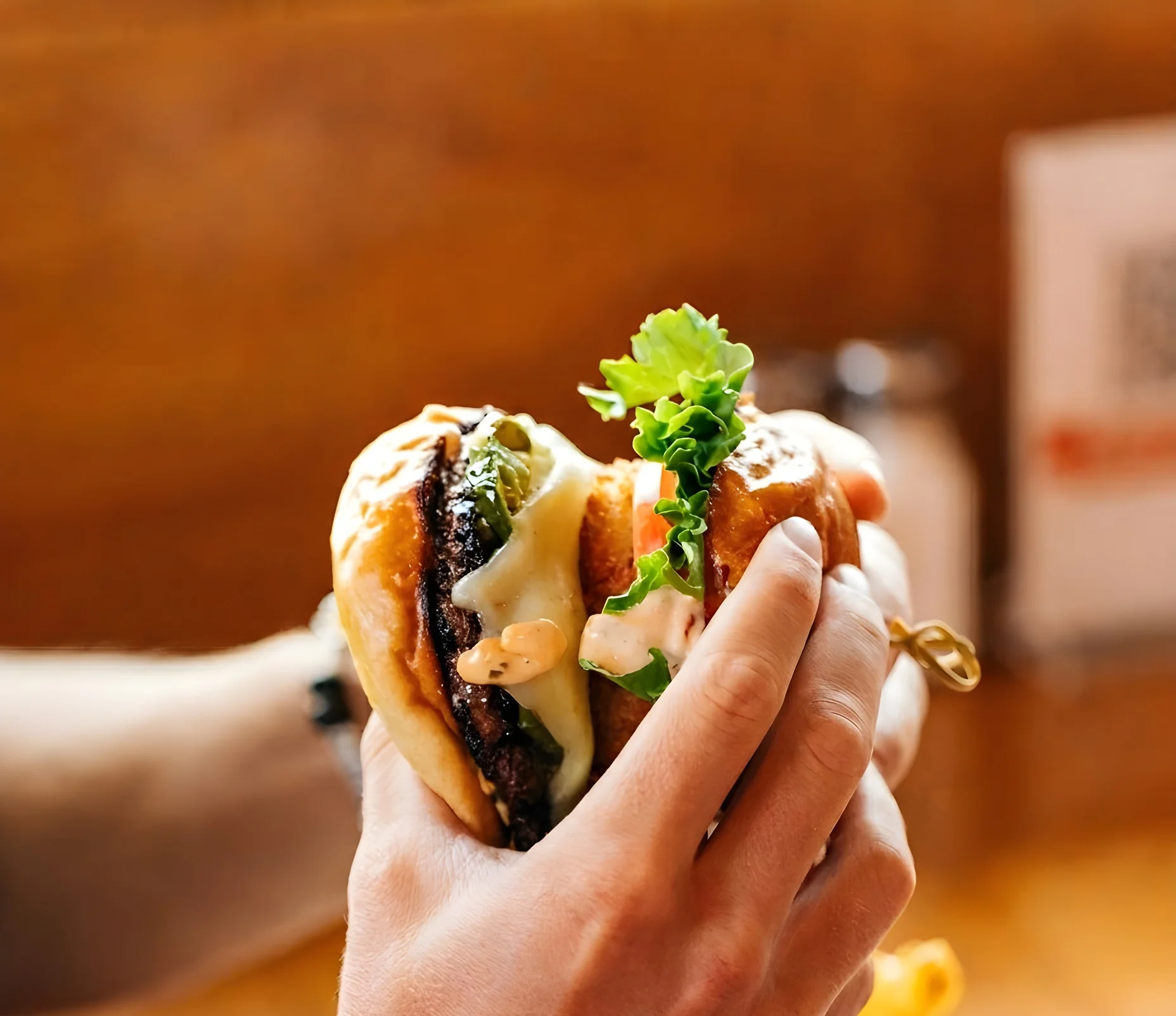 A hand holding a delicious burger with lettuce and sauce.