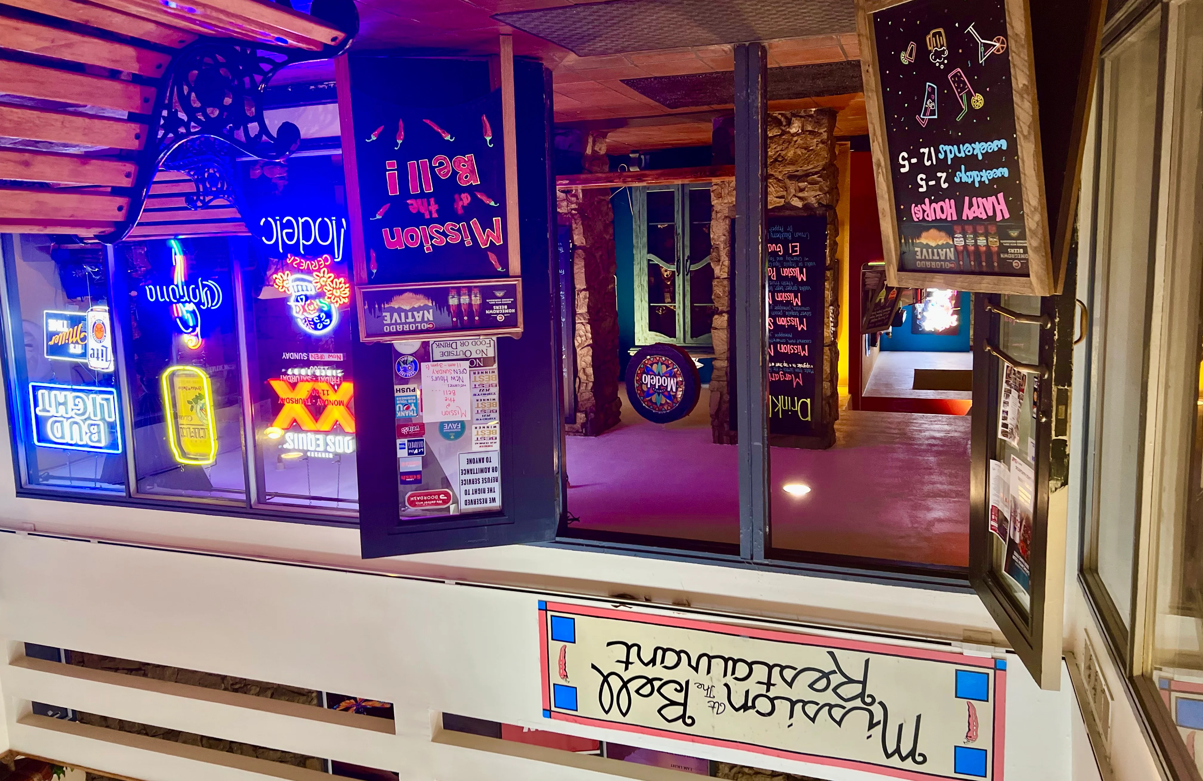 Entrance of Mission at the Bell restaurant with neon signs and happy hour board