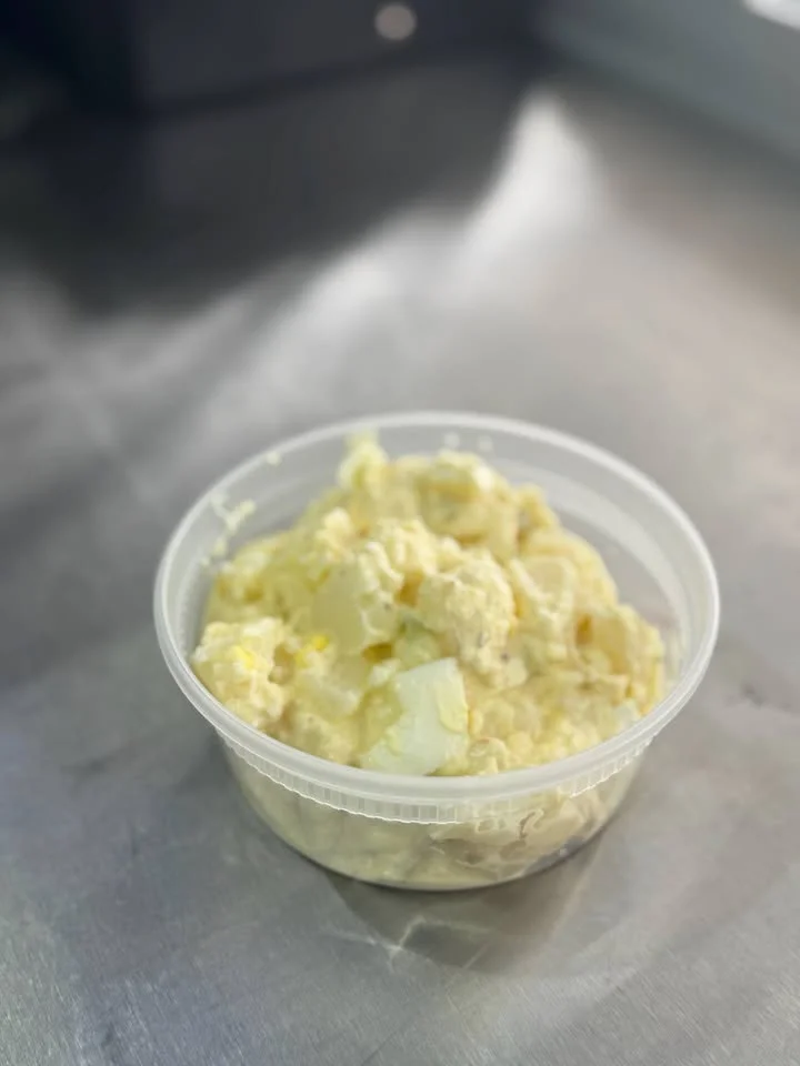 A plastic container filled with creamy potato salad, featuring diced potatoes.