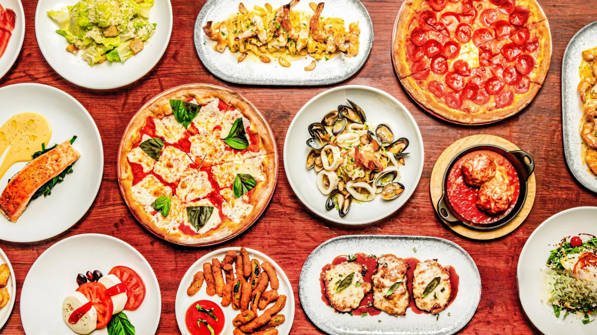 Italian feast featuring pizza, seafood pasta, and fresh salads