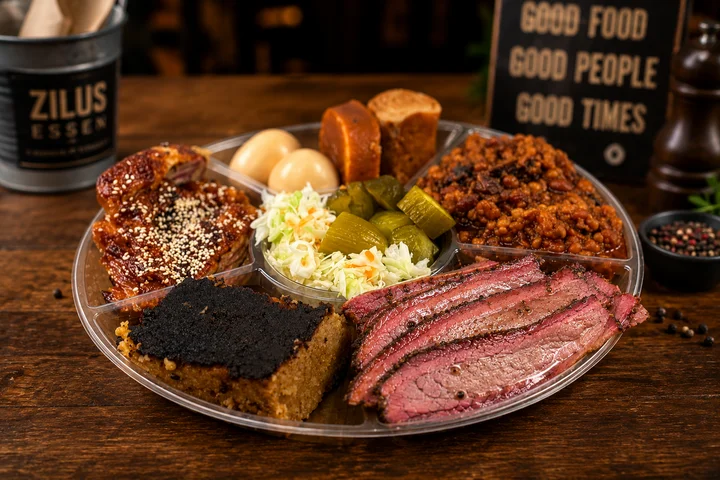 Texas barbecue platter with sliced brisket, ribs, baked beans, pickles, and cornbread