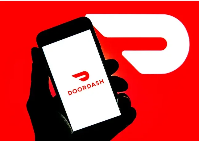 Hand holding a smartphone displaying the DoorDash app logo
