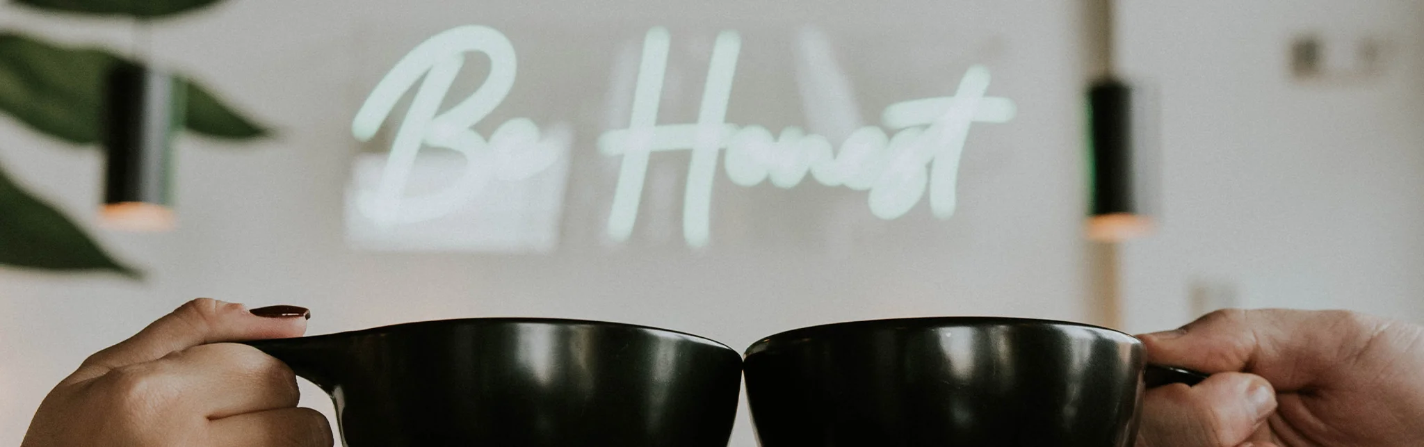 Two hands clinking black coffee mugs in a cozy cafe setting