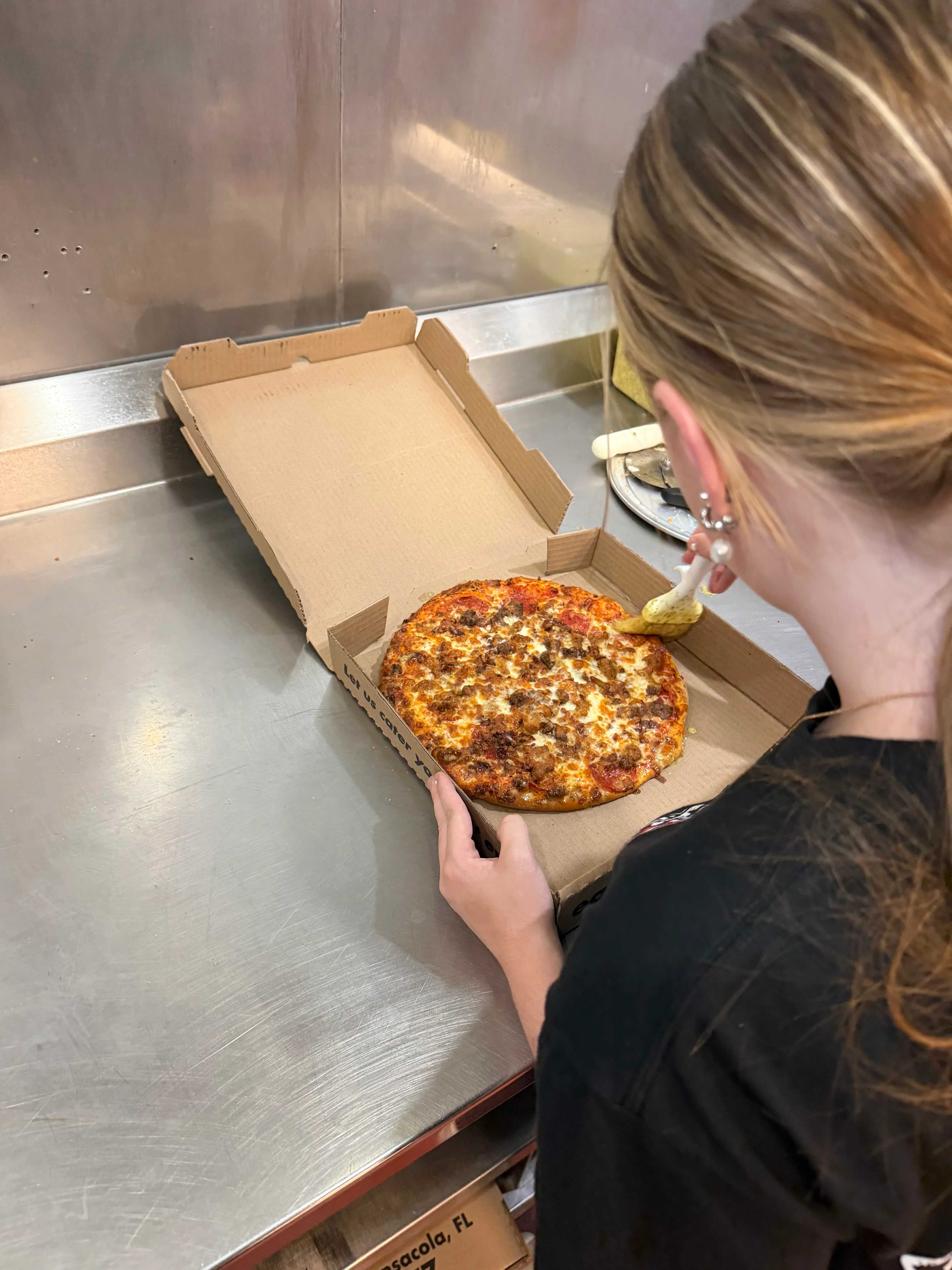 Cheesy Italian-style pizza being boxed in a restaurant kitchen