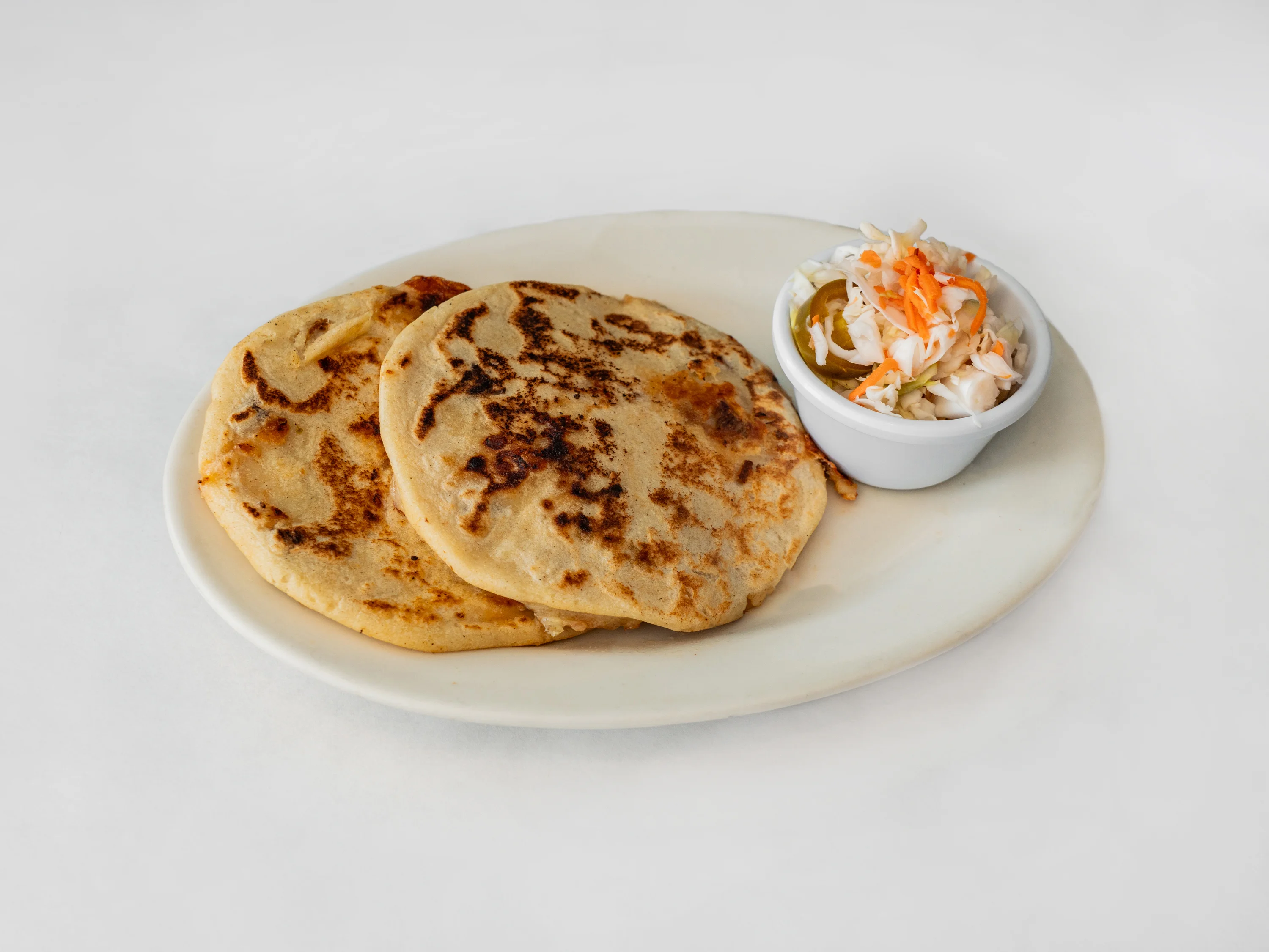A plate of pupusas, thick corn tortillas served with a side of pickled slaw.