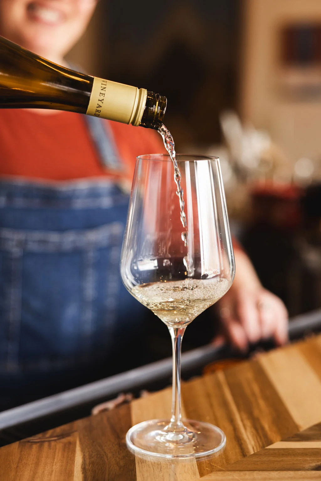 A glass is being filled with sparkling wine from a bottle, showcasing the drink's effervescence. The background features a casual bar setting.