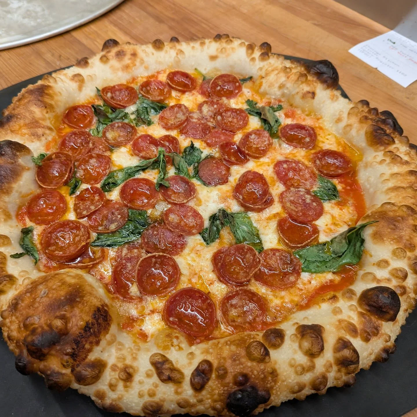 A 12 inch pizza topped with red sauce, mozzarella cheese, pepperoni, roasted garlic puree and fresh basil leaves. The crust is golden brown, micro-blistered and fluffy.