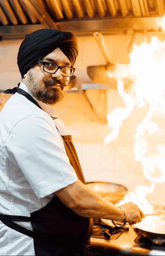 A chef overseeing a cooking process with flames in the background.