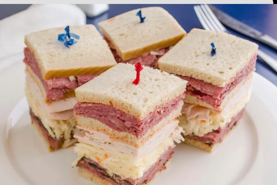 An assortment of dishes including sliced meat, salad, desserts, and sides arranged on white plates.