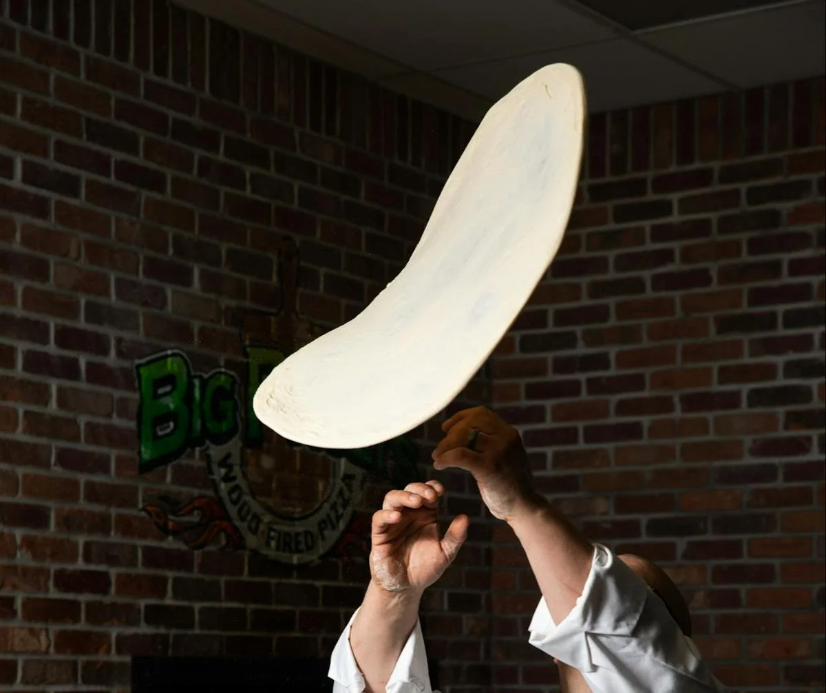 A chef hand tossing pizza dough