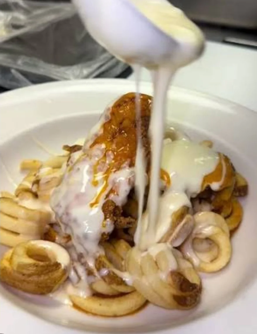 A dish with spiral pasta topped with a piece of fried chicken and drizzled with a creamy sauce.
