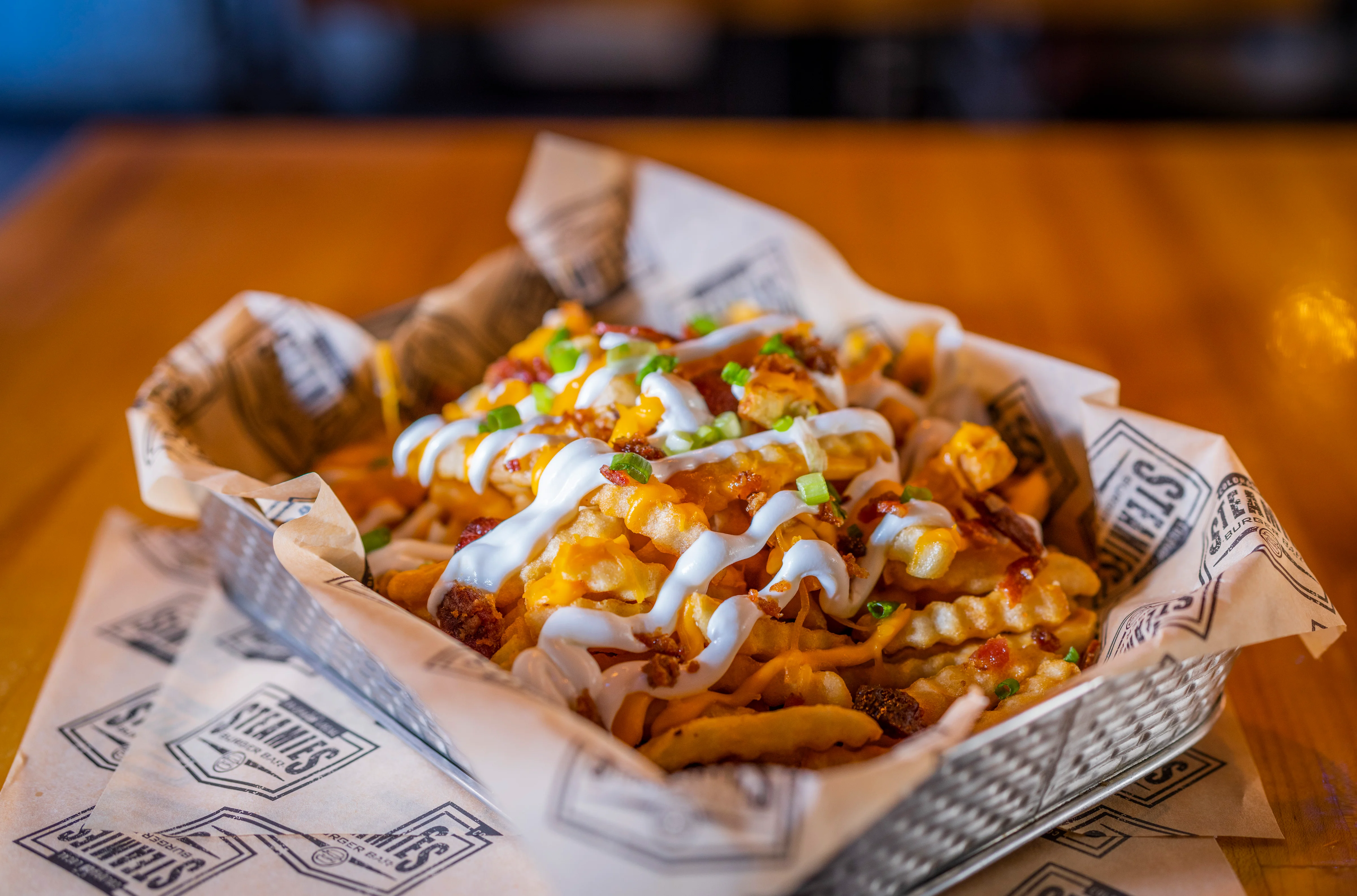 A basket of loaded fries topped with cheese, bacon bits, and sour cream, garnished with green onions.