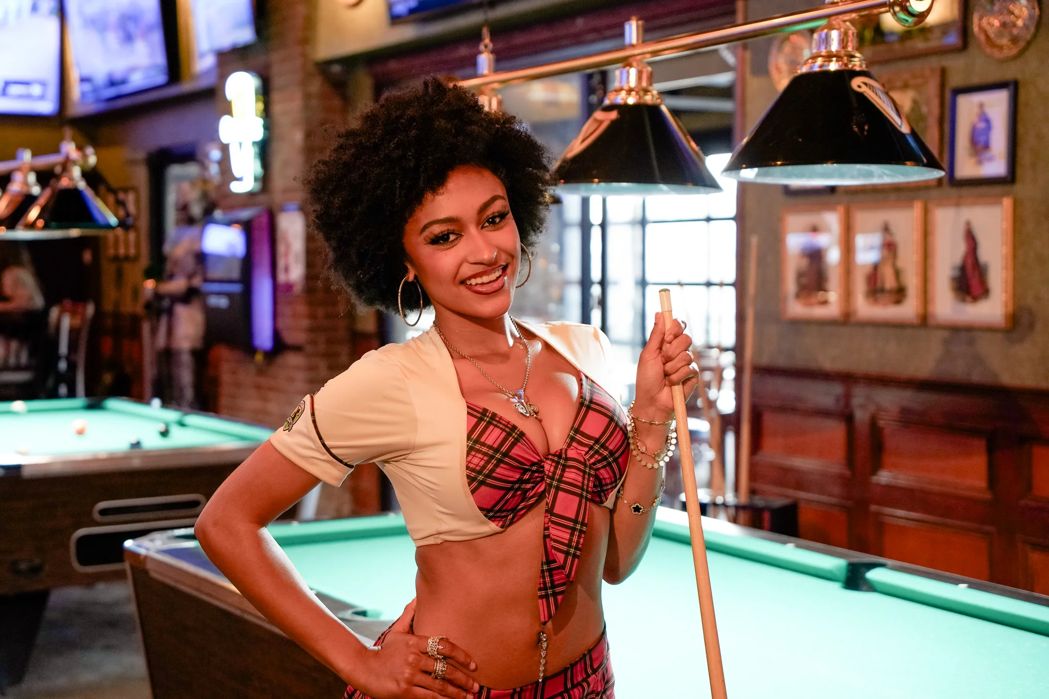 Smiling woman posing with a pool cue in a lively bar setting
