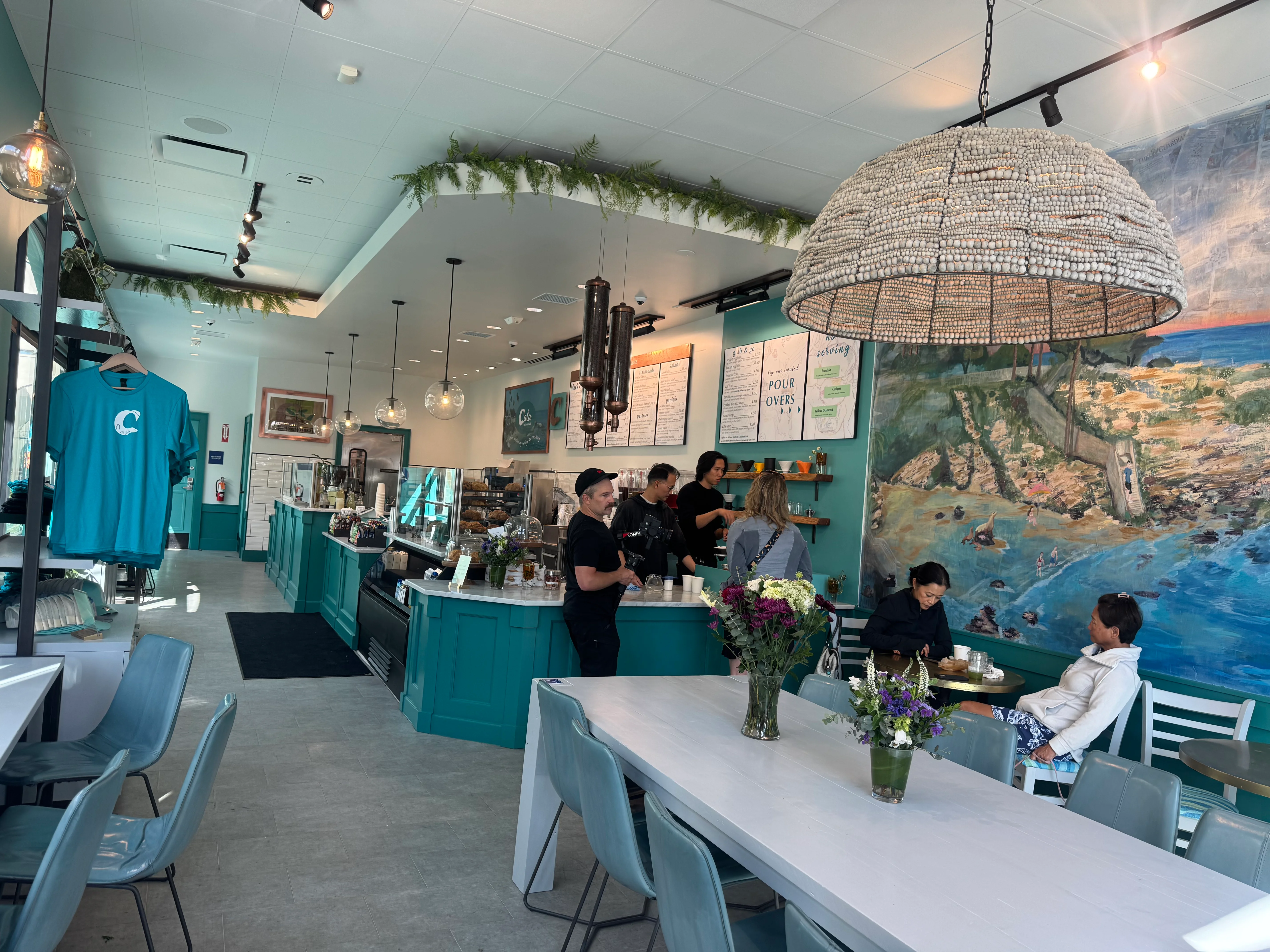 The interior of a cozy café featuring teal decor, a large mural, and an inviting atmosphere with customers enjoying their time.