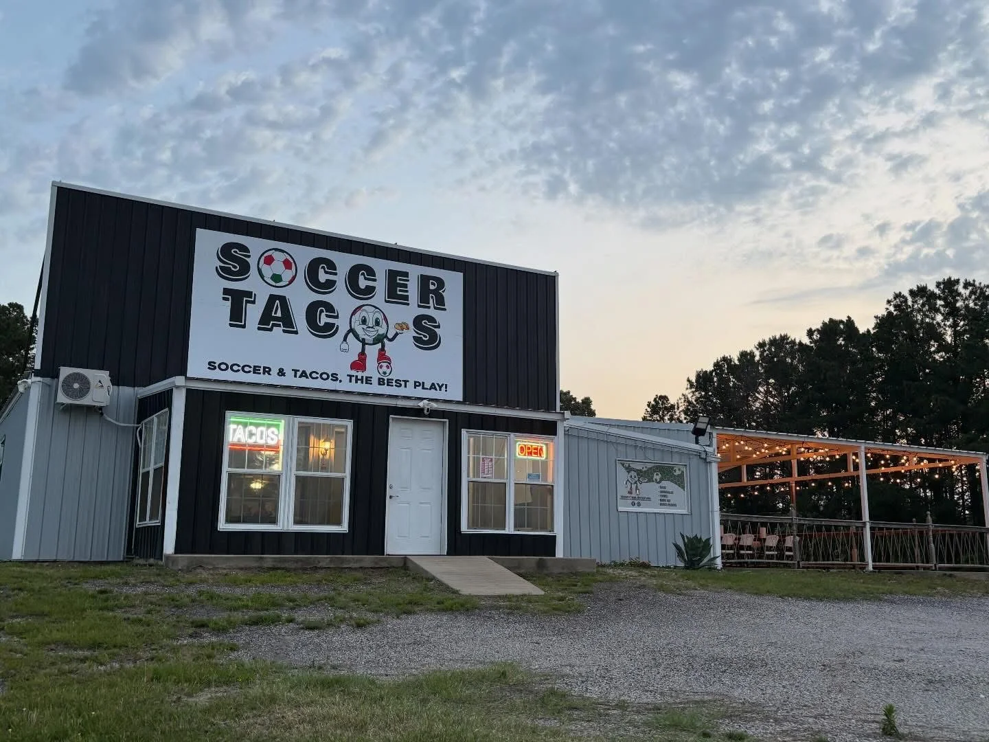 An exterior view of a restaurant named 'Soccer Tacos' with an inviting open sign and a patio area.