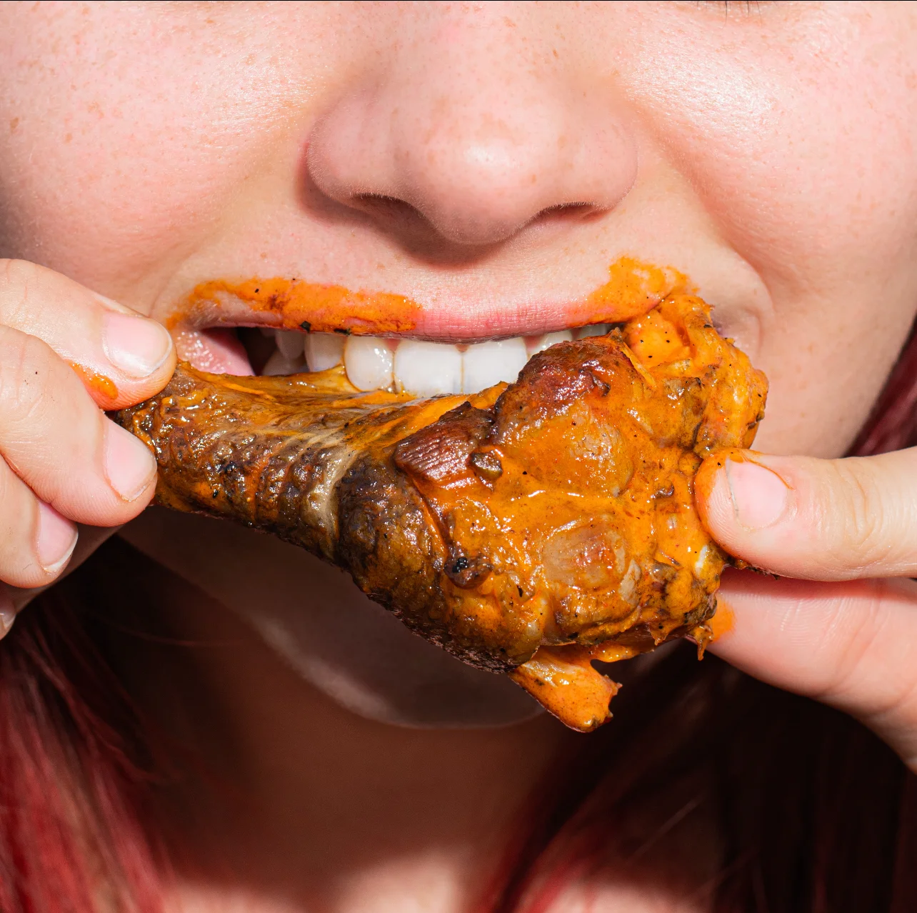 Person enjoying spicy chicken wing with sauce