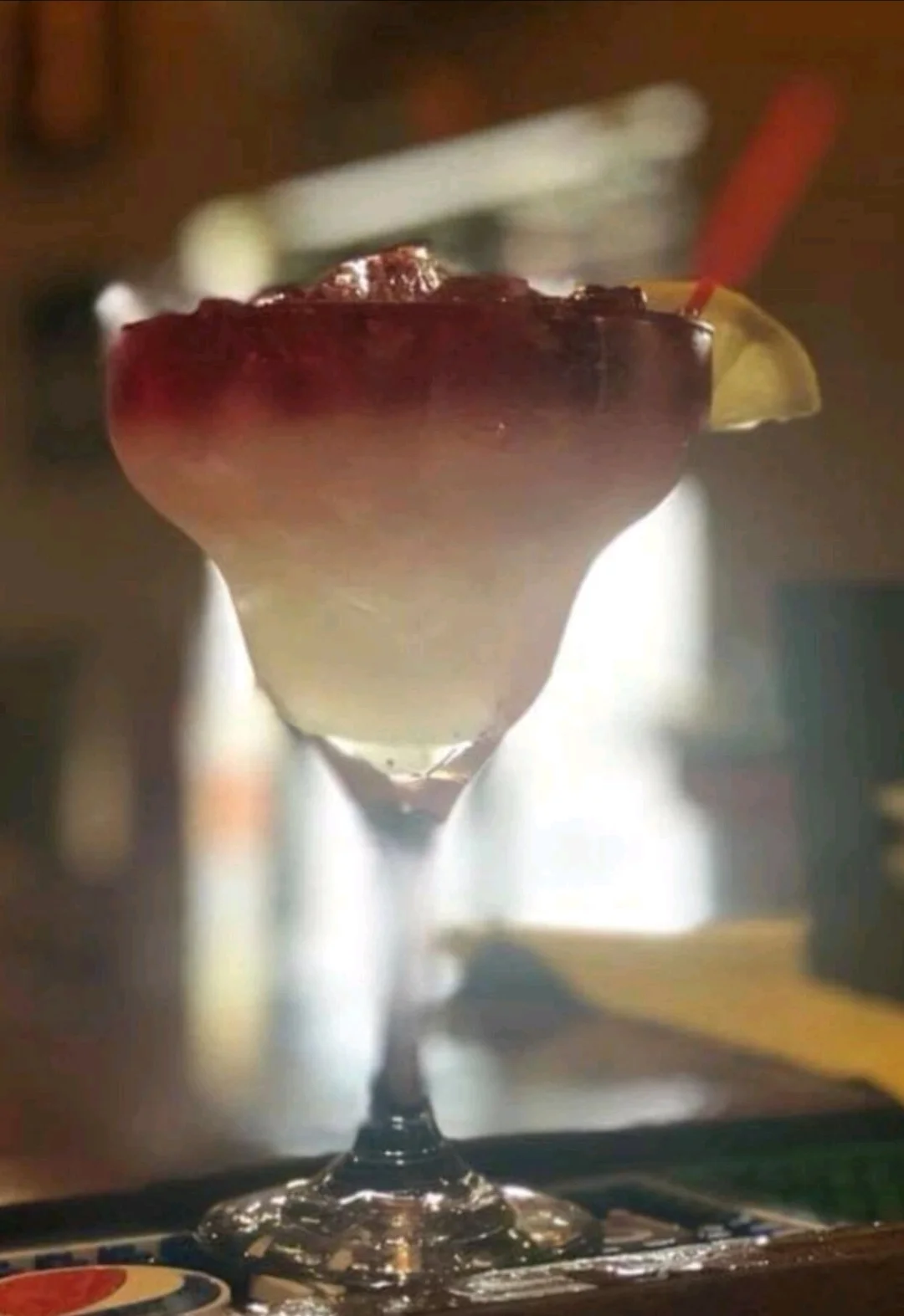 A colorful cocktail in a large glass, featuring a gradient of colors from red to white, garnished with a slice of lime.