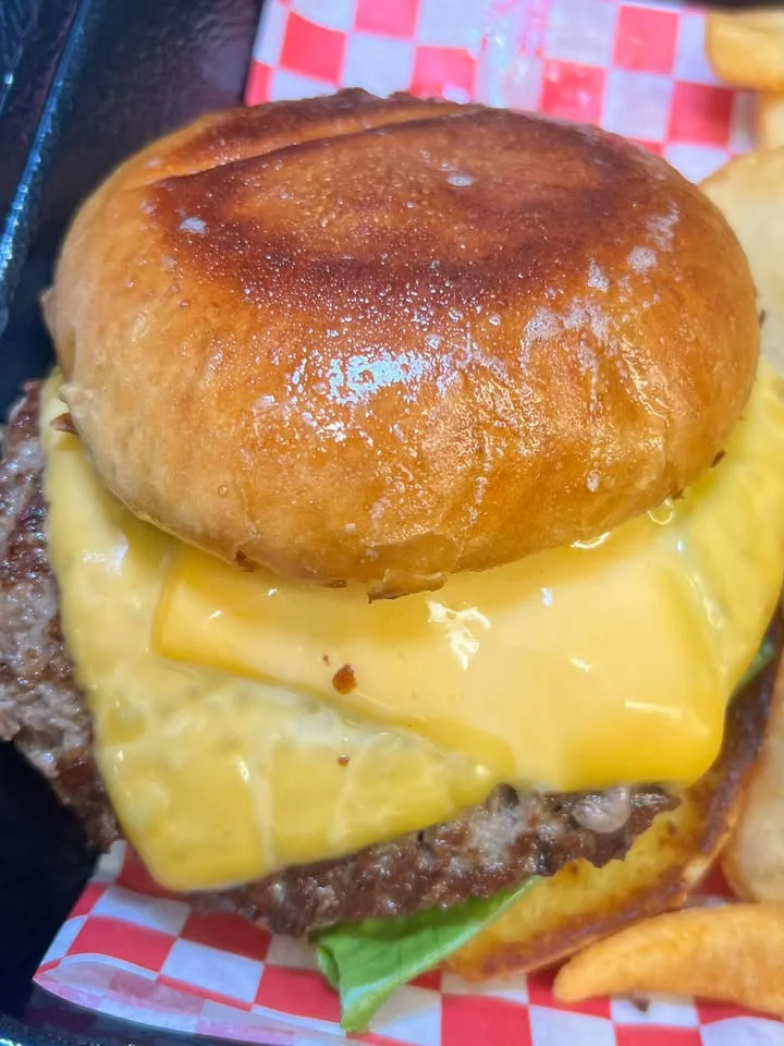 A cheeseburger on a toasted bun, topped with melted cheese, served with a side of fries.